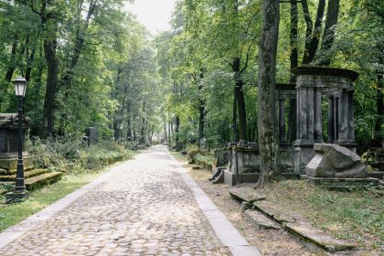 Caminho de pedras entre árvores e túmulos em um cemitério ao ar livre.